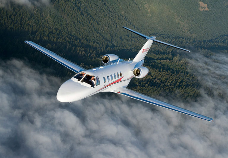 Cessna Citation CJ2+ from Bloom Business Jets in flight over clouds and trees.