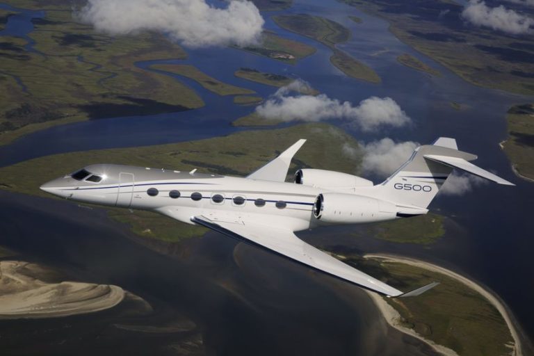 Gulfstream G500 from Bloom Business Jets in flight in clouds above land and water.